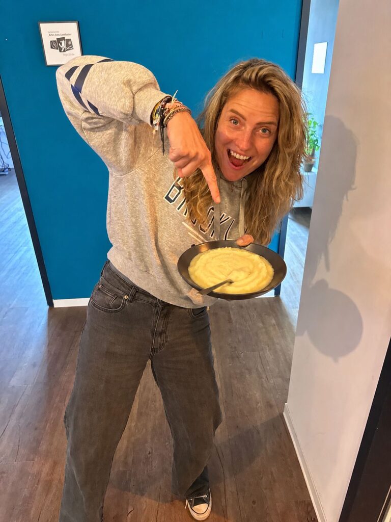 Isabell zeigt lachend auf einen Teller Kartoffelbrei.